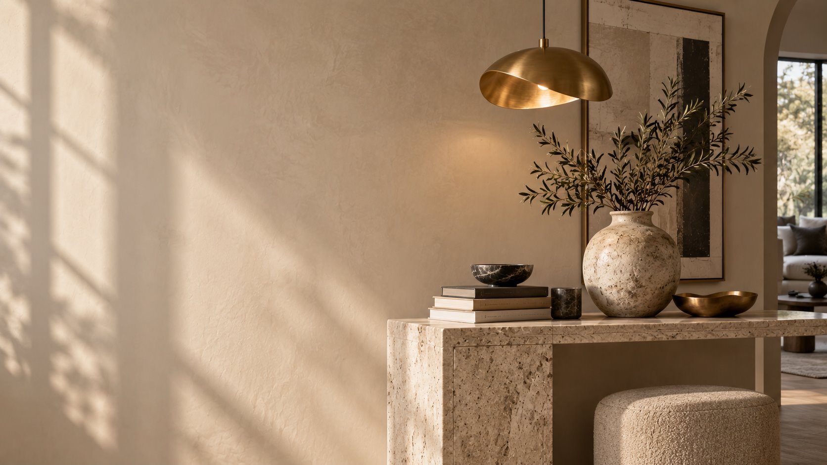 Warm minimalist interior with a brass pendant lamp and a ceramic vase on a travertine console